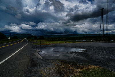 Road passing through landscape against storm clouds