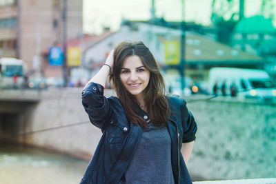 Portrait of beautiful woman with hand in hair standing at city