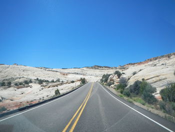 Road leading towards mountains against clear blue sky