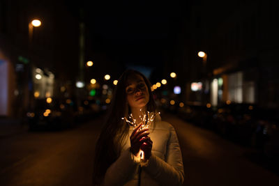 Portrait of woman standing on illuminated street at night