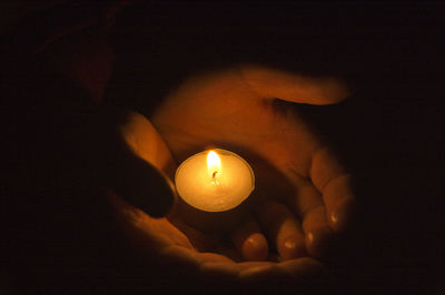 Close-up of hand holding lit candle in the dark