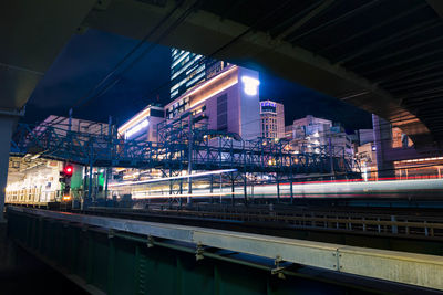 Illuminated bridge by buildings against sky at night