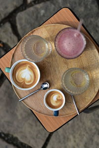 Cappuccino, macchiato, raspberry lemonade and two water glasses on a wooden tray,  in a public park