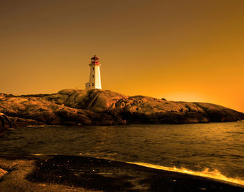 Lighthouse by sea against sky during sunset