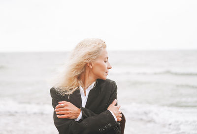 Portrait of elegant blonde woman in black suit near sea in a storm