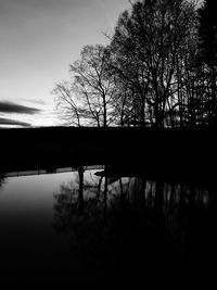 Silhouette bare trees by lake against sky during sunset