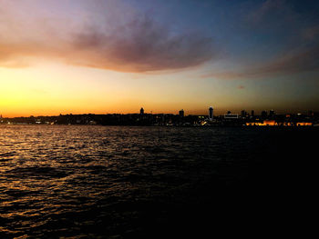 Silhouette buildings by sea against sky during sunset
