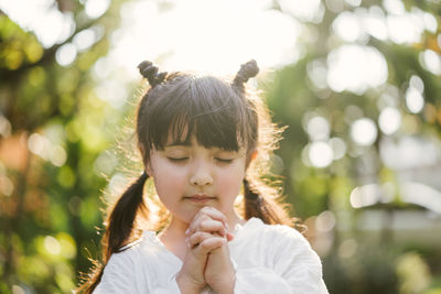 Cute girl praying while standing in park