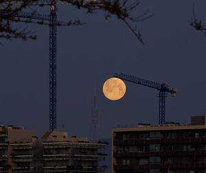 Low angle view of crane and buildings against sky at night