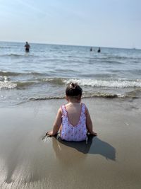 Rear view of woman sitting at beach against sky