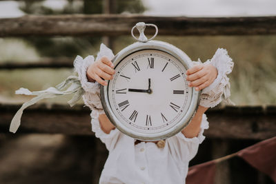 Close-up of person holding clock against white wall