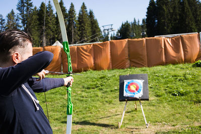 Man using bow and arrow and shooting at the target outdoors.