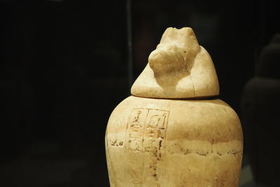 Close-up of egyptian canopic jar on table against black background