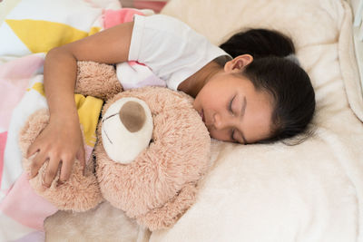 High angle view of girl with teddy bear sleeping on bed at home