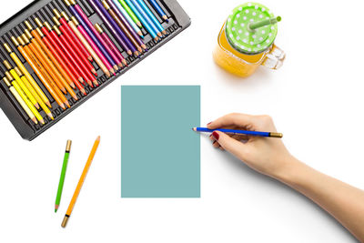 Cropped image of hand holding colored pencils against white background