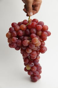 Close-up of hand holding grapes over white background