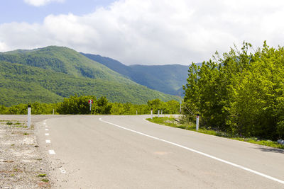 Empty road along trees and mountains against sky