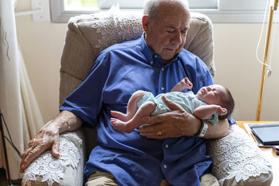 Grandfather sitting in an armchair holding a newborn baby