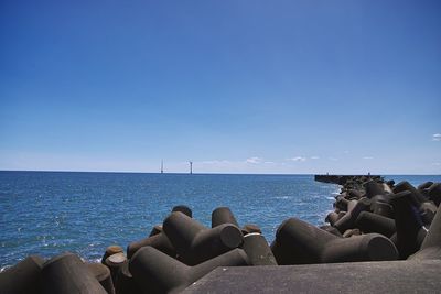 Man sitting on rocks by sea against clear blue sky