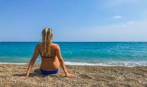 Rear view of woman sitting at beach against sky