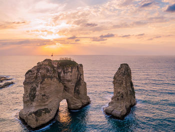 Rock formation in sea against sky during sunset