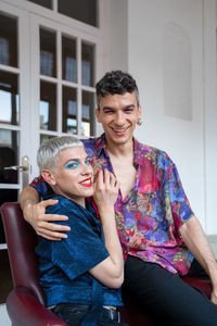 Portrait of smiling and loving gay couple sitting on armchair at home