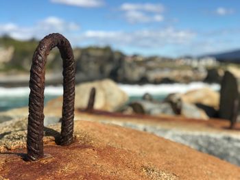 Close-up of rusty metal on rock at beach against sky