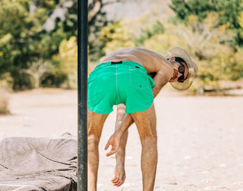 Rear view portrait of shirtless man bending outdoors