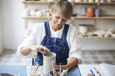 Mature woman molding earthenware at table in art class