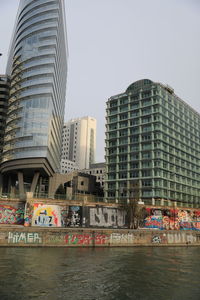 Modern buildings by river against clear sky