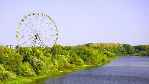Ferris wheel by lake against clear sky