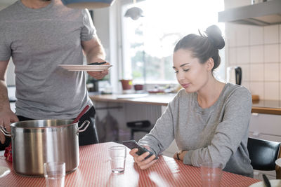 Midsection of father holding plate while daughter using smart phone at dining table in kitchen