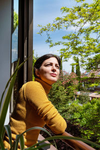 Thoughtful woman standing by railing against plants