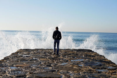 Rear view of man standing at pier by sea