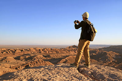 Man photographing on rock against clear sky