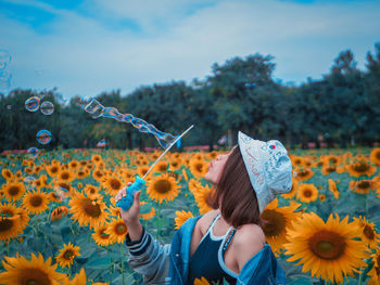 Young woman blowing bubbles amidst flowering sunflowers