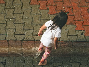 Full length of woman on footpath against brick wall