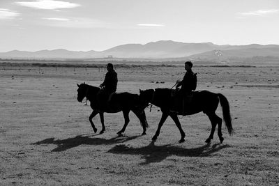 Silhouette people riding horses on mountain against sky