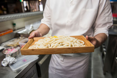 Midsection of chef holding tray of noodles