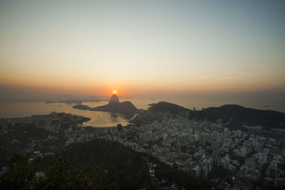 Cityscape by sea against clear sky during sunset