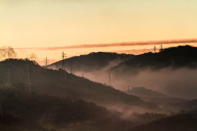 High angle view of electricity pylons on mountains against sky during sunset