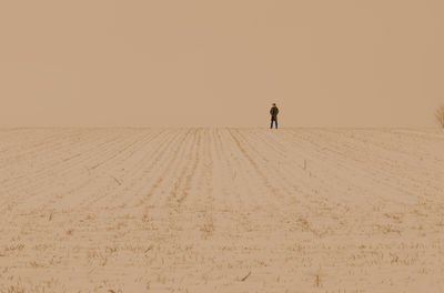 Minimalistic distant silhuette of a man at horizon over wide grassland slightly powdered with snow