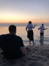 Rear view of people on beach against sky during sunset