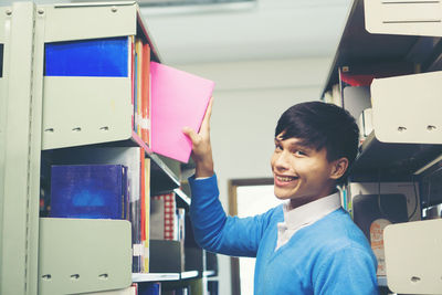 Portrait of smiling man removing book from shelf in library