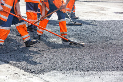 Road workers in orange reflective uniforms level fresh asphalt with metal levels on  stretch of road