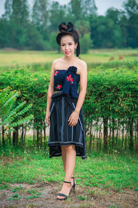 Portrait of beautiful young woman wearing dress while standing on field against plants