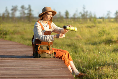 Naturalist woman resting on boardwalk, drinking tea, enjoying the moment at sunset. ecotourism