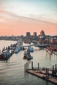 Boats in harbor by buildings against sky during sunset