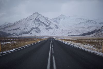 Empty road leading towards mountains against sky