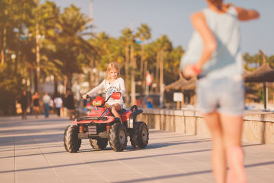 Girl riding toy car on footpath